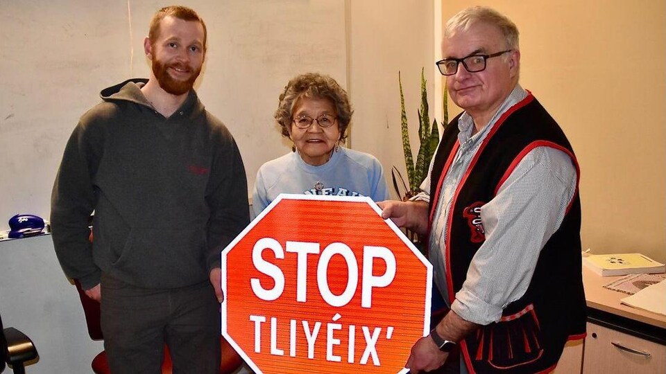 Trois personnes tiennent un panneau routier « arrêt » en anglais et tlingit.
