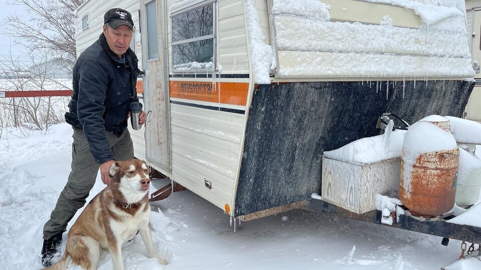 Un homme et son chien devant leur campeur, alors que le paysage est recouvert de neige.