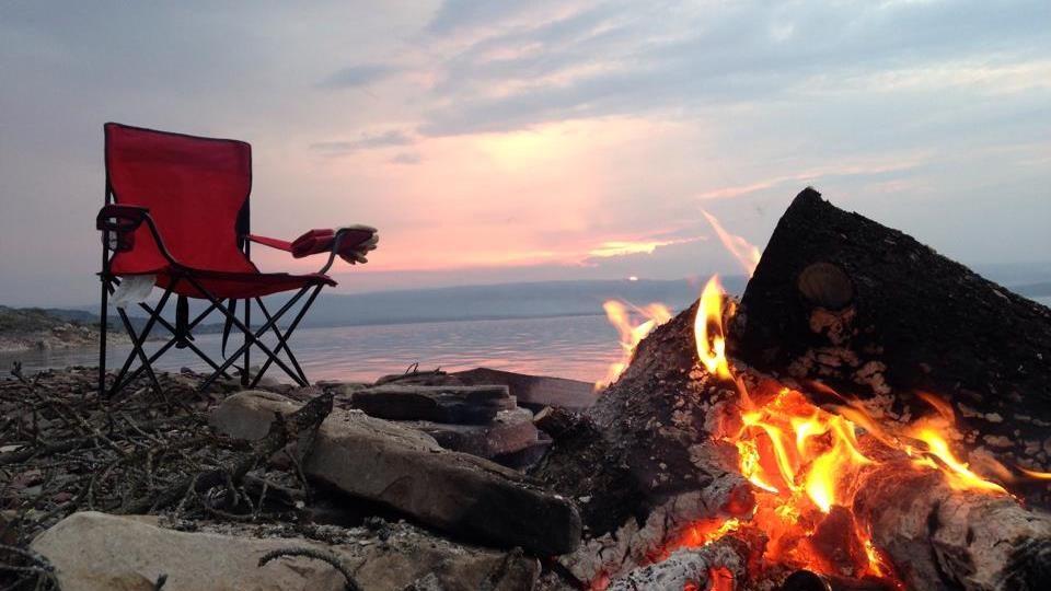 Un feu sur une plage au soleil couchant, avec une chaise de camping installée non loin.