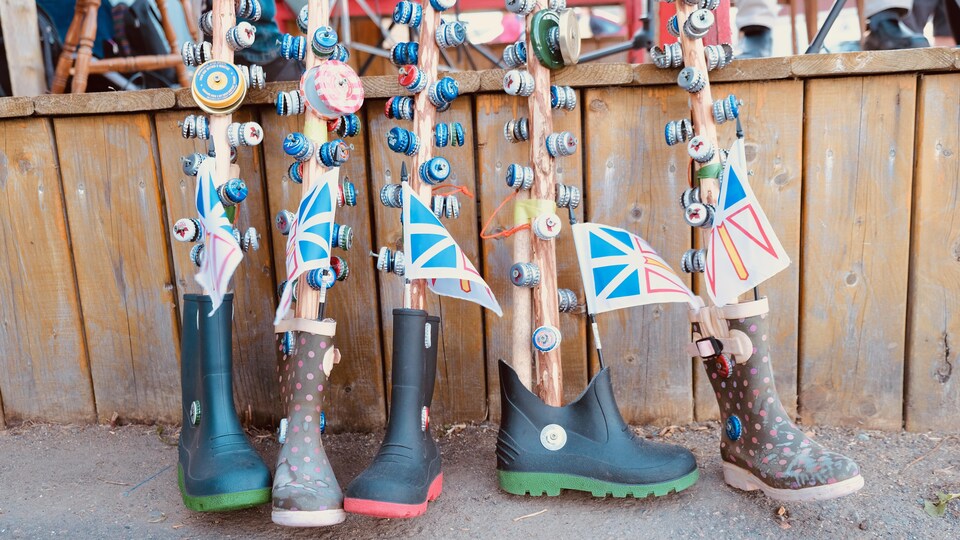 Des bâtons décoratifs et des petits drapeaux de Terre-Neuve-et-Labrador sont plantés dans cinq bottes de caoutchouc appuyées contre une estrade en bois, à l'extérieur lors d'une fête communautaire.