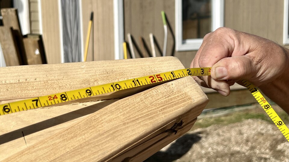 Une main tient un ruban à mesurer sur un morceau de bois, à Fort Smith, en septembre 2022.