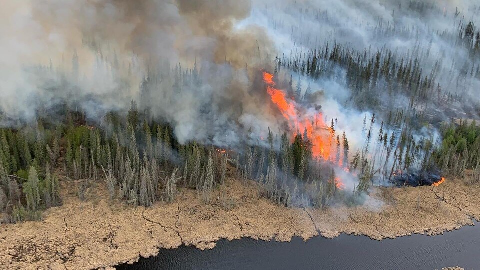 Feu de forêt avec fumée et flammes, près d'une rivière, le 15 mai 2023, à Hay River, aux Territoires du Nord-Ouest.