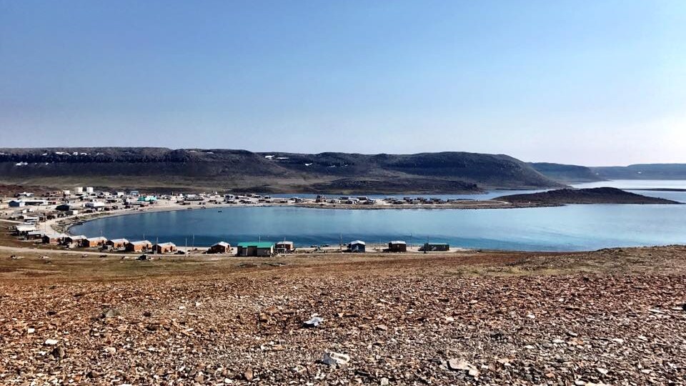 Une rangée de maisons autour d'une baie et des collines au loin l'été.