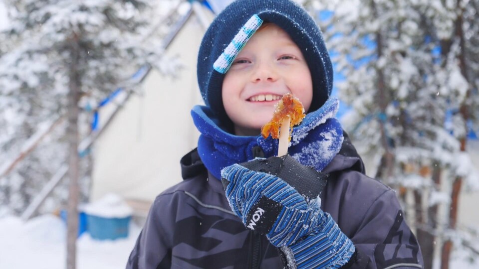 Enfant avec tuque, foulard et manteau d'hiver avec tire d'érable sur un bâton, le 30 novembre 2022, à Yellowknife.