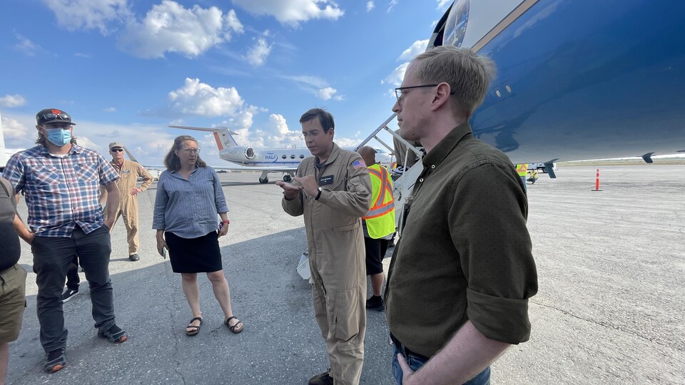 Un scientifique portant un vêtement de travail au logo de la NASA se tient devant un avion et parle à un groupe de participants lors d'un événement portes ouvertes, à Yellowknife, le 16 août 2022.