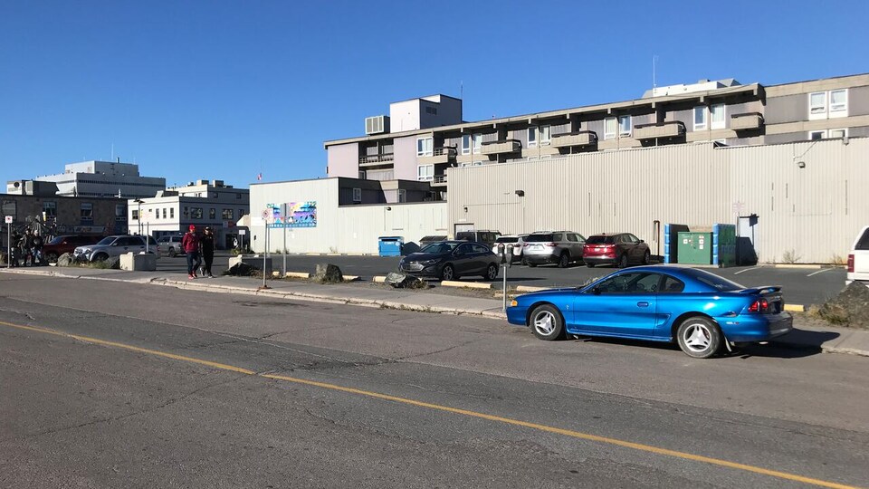 Édifice et rue au centre-ville de Yellowknife, avec une voiture stationnée le long d'un terrain vacant.