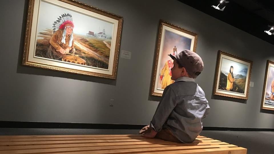 Un jeune garçon sur un banc regarde les toiles de chefs autochtones