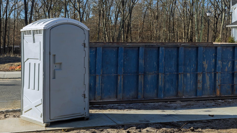 Une toilette chimique près d'un conteneur bleu.