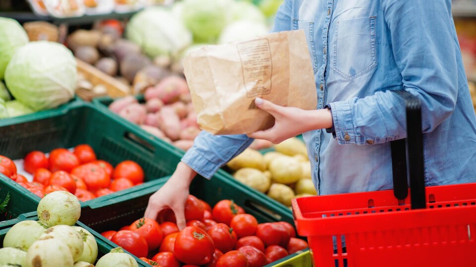 Une femme prend une tomate dans une épicerie.