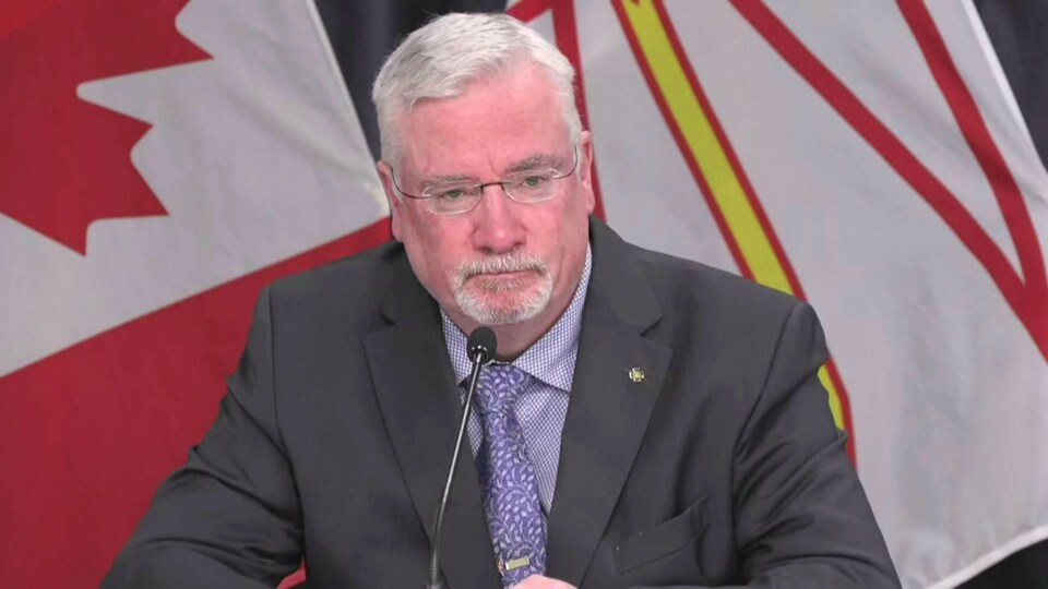 Tony Stack assis en conférence de presse devant un drapeau du Canada et un drapeau de Terre-Neuve-et-Labrador.