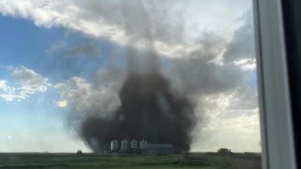 Photo prise derrière une fenêtre d'une tornade proche d'une exploitation agricole.
