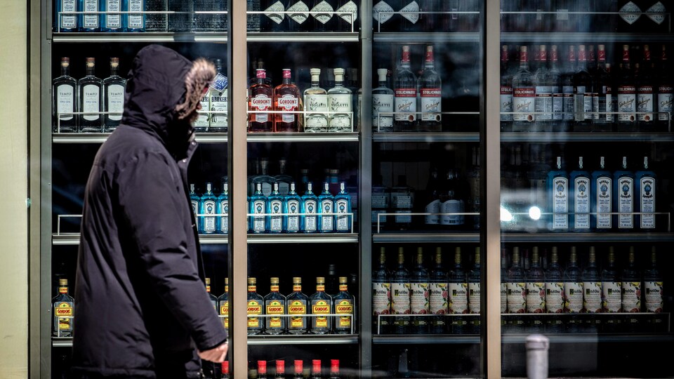 Un homme marche devant un magasin de vente d'alcool.