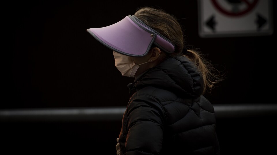 Une personne portant un masque et un chapeau à large visière marche dans la rue.