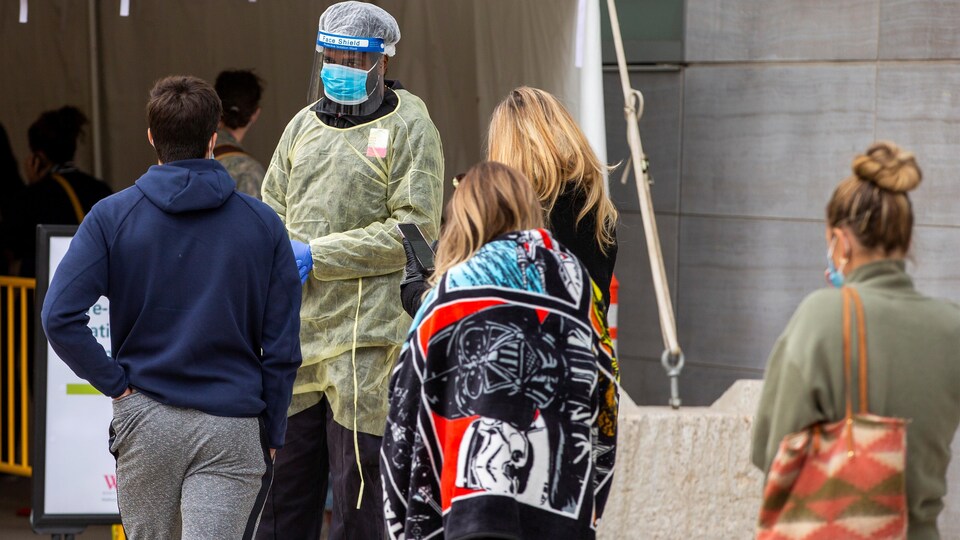 Des gens attendent en ligne devant une clinique.