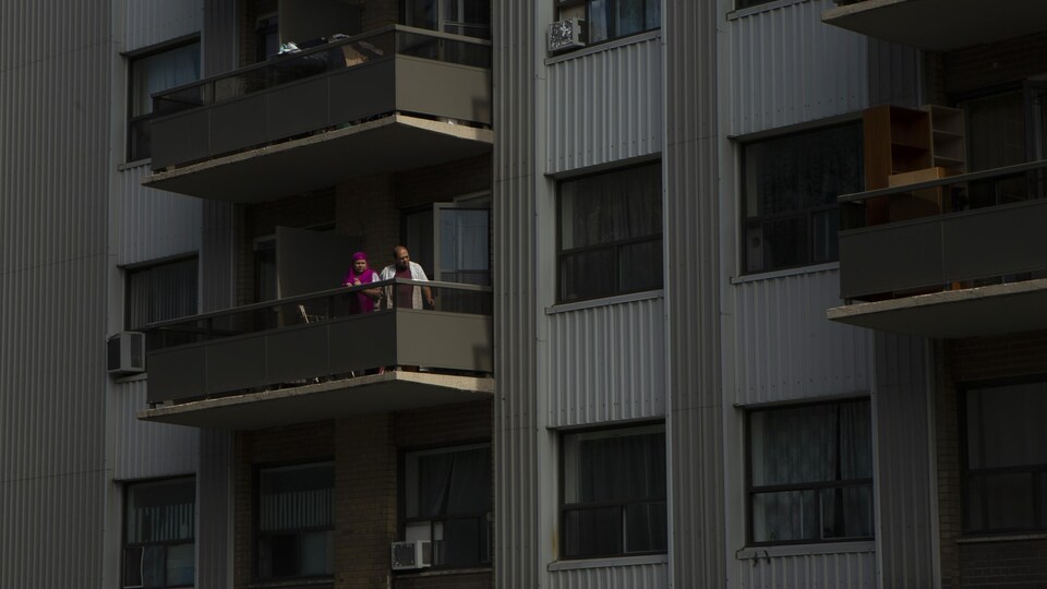 Un couple regarde à l'extérieur depuis le balcon de son appartement.