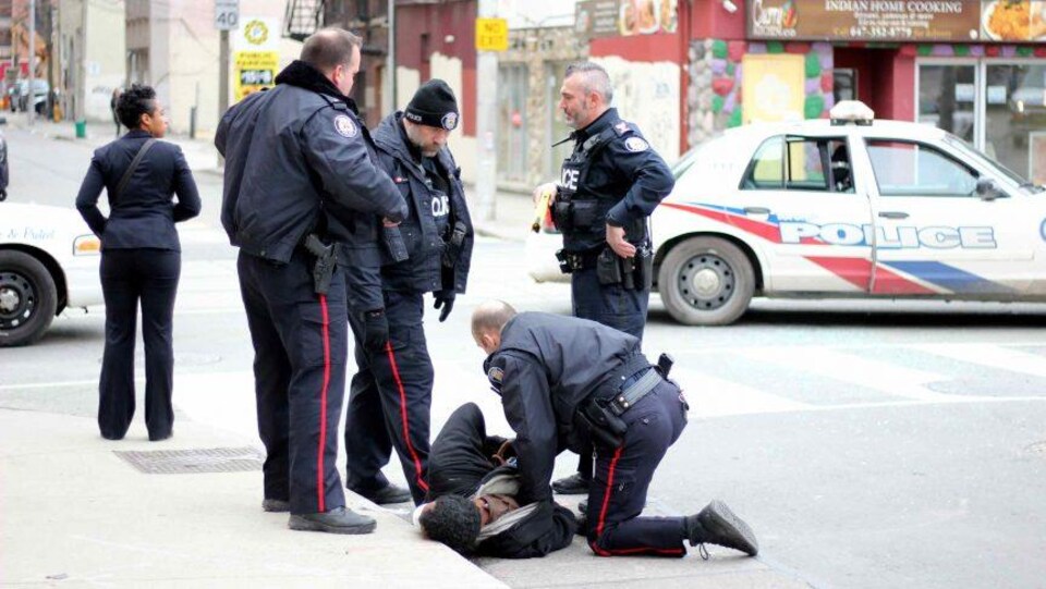 Des policiers tentent de maîtriser un homme noir qui est allongé au sol.