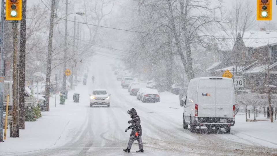 Une personne traverse la rue pendant une tempête de neige.