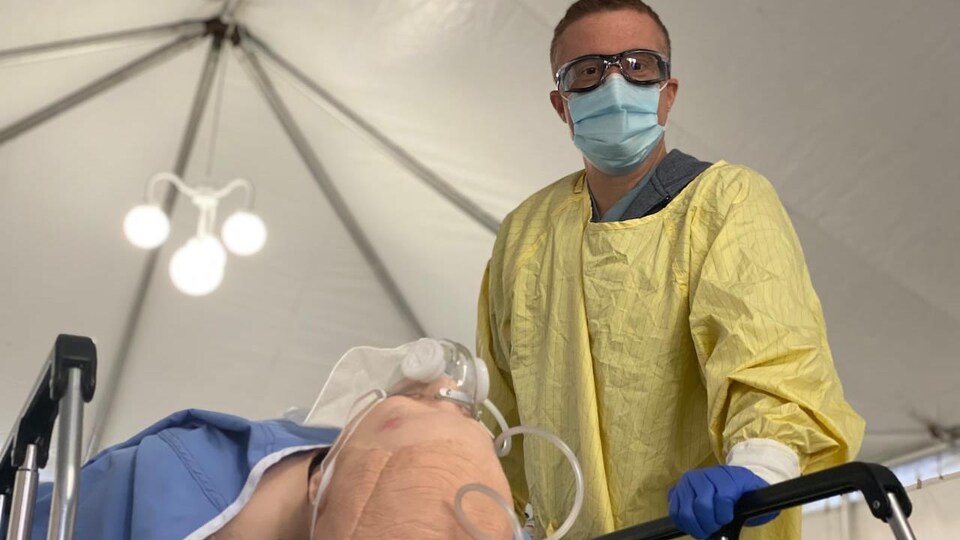 L'infirmier Brad Poechman près d'un mannequin sur une civière qui a un masque à oxygène.