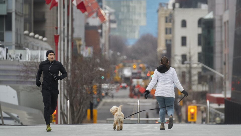 Un homme qui court dans la rue sous l'oeil d'un caniche en laisse.