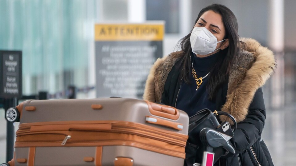 Une voyageuse portant un masque pousse un chariot rempli de valises à l'aéroport Pearson.