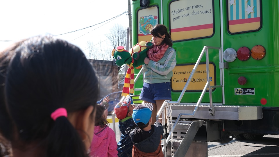 Une comédienne avec une marionnette parle devant des enfants à l'extérieur. 