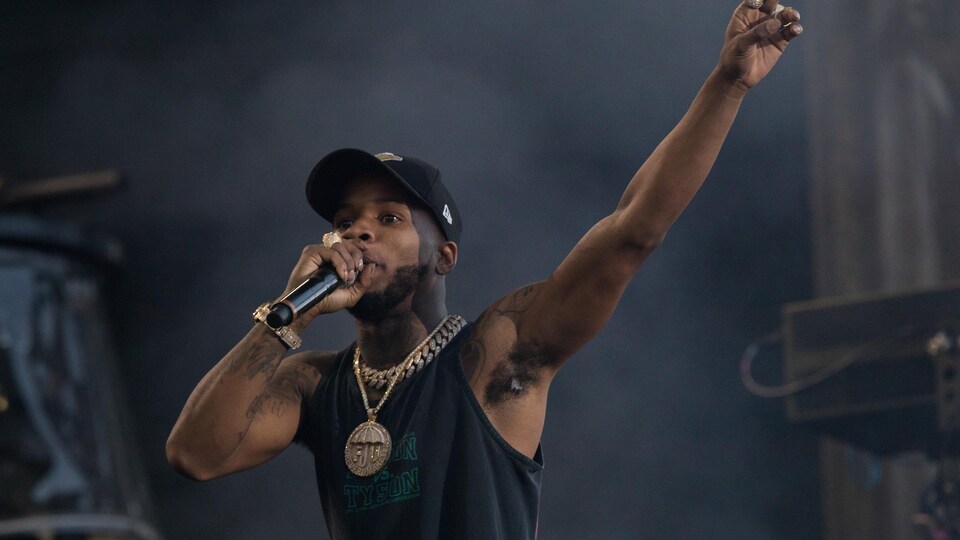 Tory Lanez, sur scène, tient un micro dans la main et lève le bras opposé.