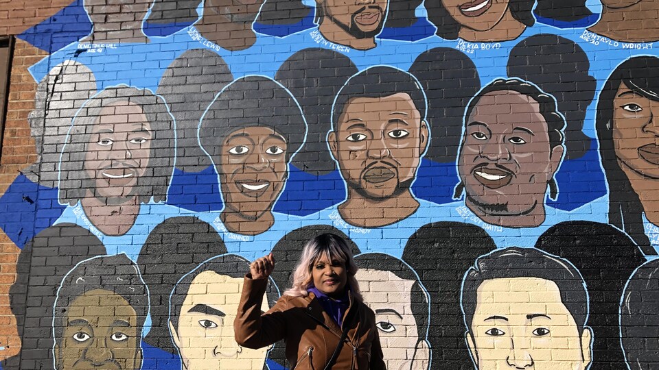 Toshira Garroway devant un mur peint sur lequel on peut voir des visages.