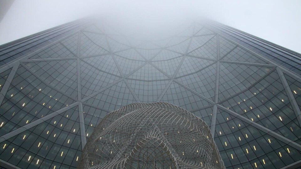 La tour Bow prise en contre-plongée, avec une statue au premier plan et du brouillard au sommet.