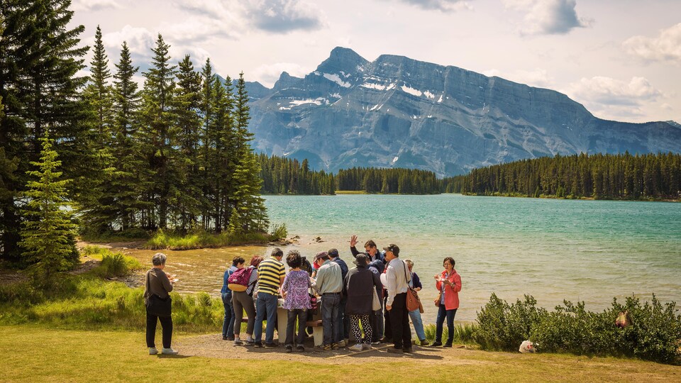 Des touristes visitent le parc national Banff. Ils se tiennent devant le lac Two Jack. Au loin s'élève le mont Rundle.