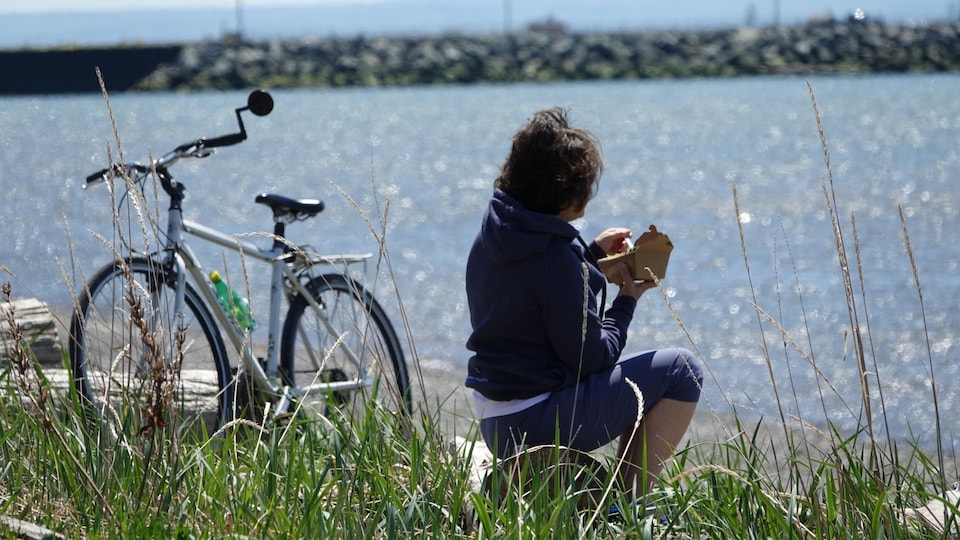 A woman on a bicycle stopped to eat while looking out to sea.