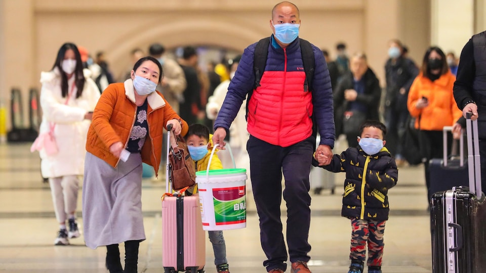 Les membres d'une famille chinoise munis de masques portent des valises.