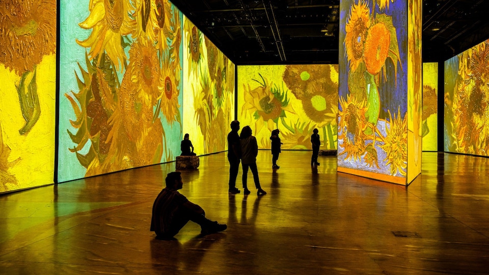 Des spectateurs dans une salle où sont projetées des toiles du peintre Vincent Van Gogh.