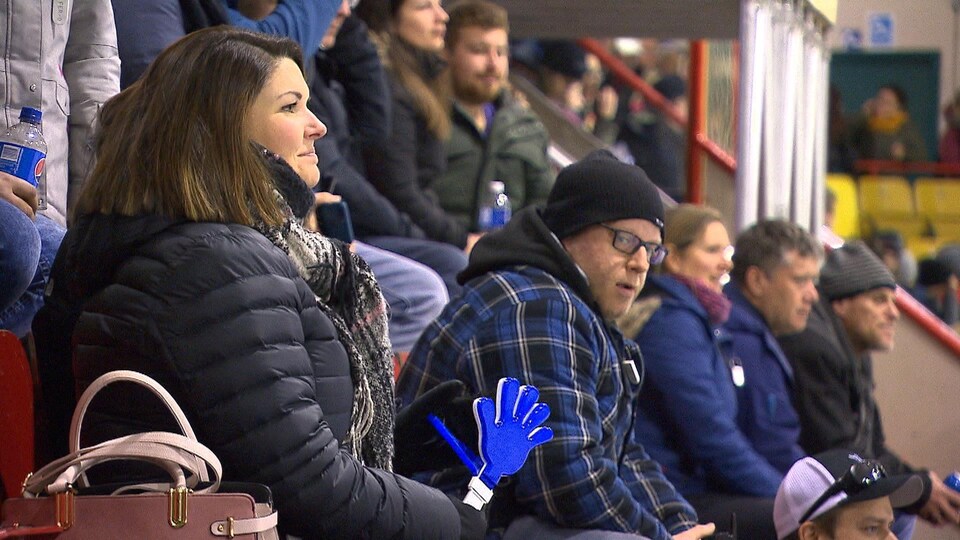 Des adultes regardent un match de hockey dans les gradins d'un aréna.