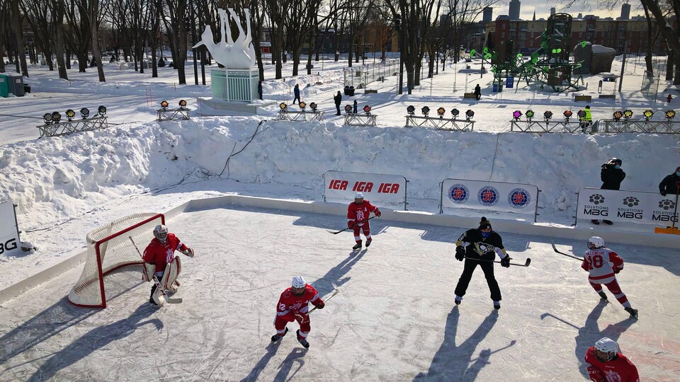 Les joueurs jouent sur la patinoire extérieure, le parc boisé derrière eux.