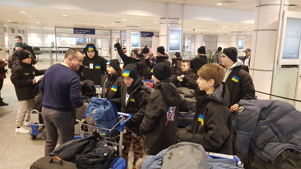 Sean Bérubé est entourée des jeunes et de leurs valises. Ils sont dans le hall d'entrée de l'aéroport de Montréal.