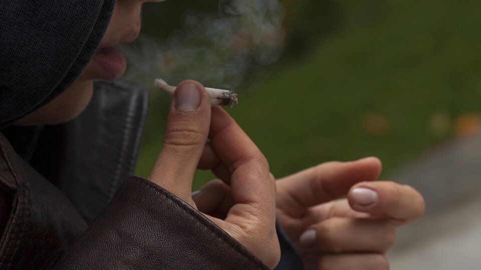 Une femme dont on ne voit qu'une partie du côté droit du visage fume ce qui semble être un joint.