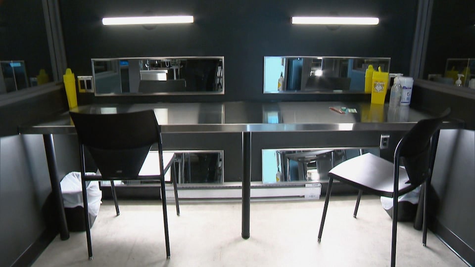 Une salle d'injection où sont disposés des seringues et des contenants à déchets sur une table stérile en aluminium.