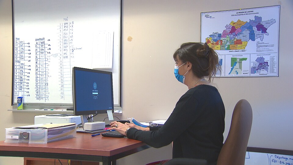 Une femme portant un masque assise devant un ordinateur.