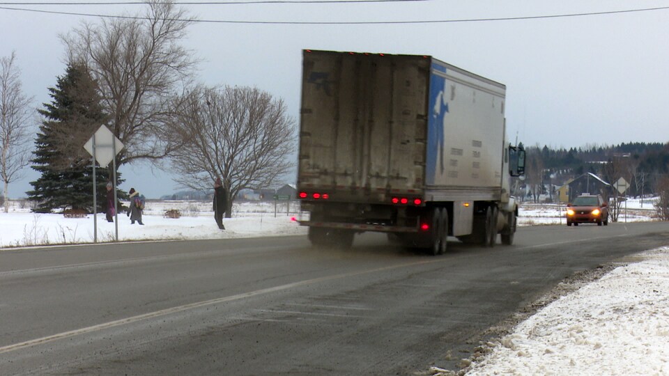 Un père et ses enfants regardent un camion passer sur la route 132.