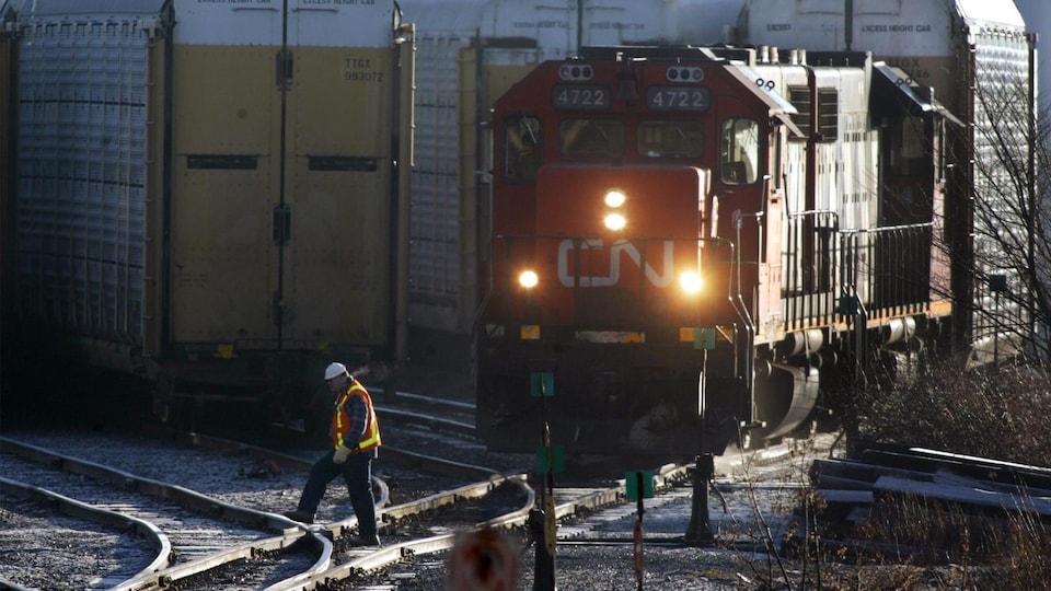 Un travailleur ferroviaire traverse une voie ferrée devant une locomotive du CN dans une gare de triage.