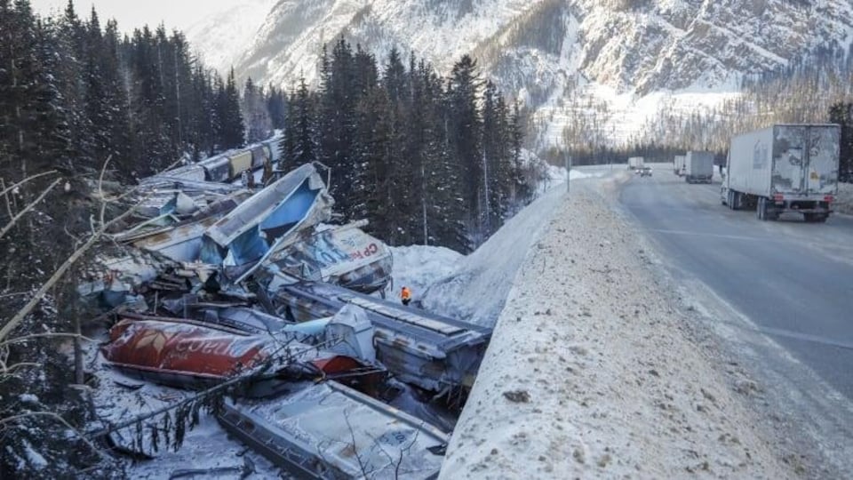 Une dizaine de wagons brisés sont empilés sur le bord d'une route enneigée.