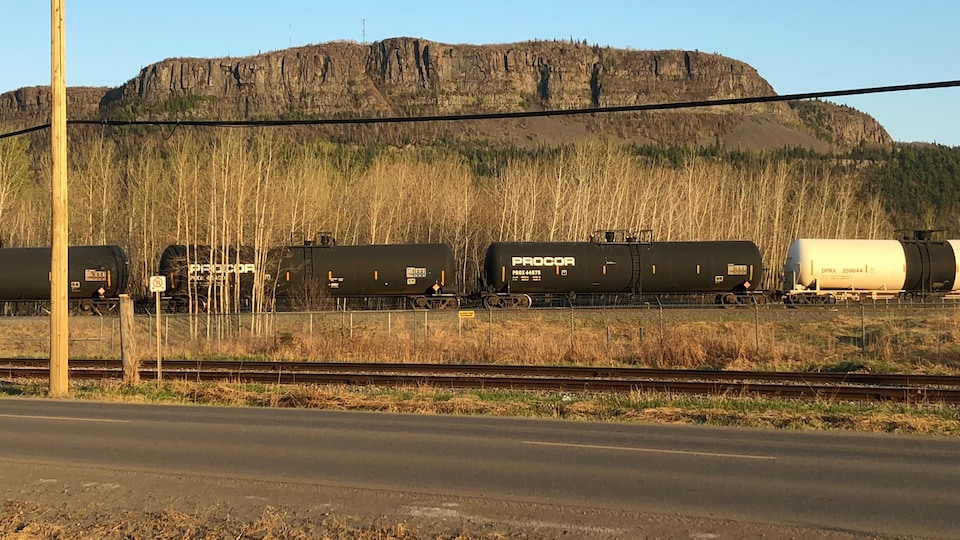 Un train de marchandises sur une voie ferrée avec une montagne derrière.