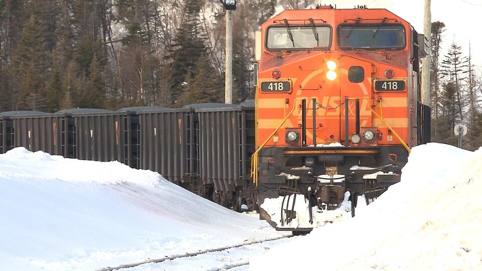 Un train transportant du minerai circule sur le rail enneigé.