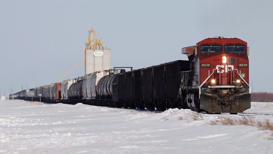 Un train de marchandises en hiver proche d'un silo de grains.