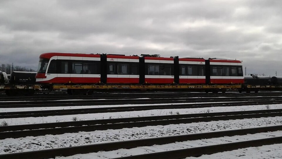Un tramway chargé sur un train dans une gare de triage.