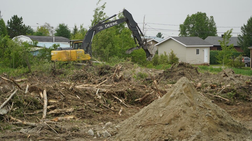 Une machine creuse le sol devant une maison.