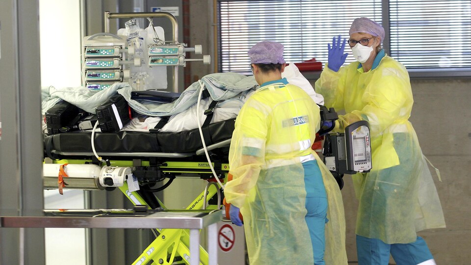 Une ambulancière fait un signe de la main pendant qu'elle pousse avec une collègue une civière dans un couloir de l'hôpital.