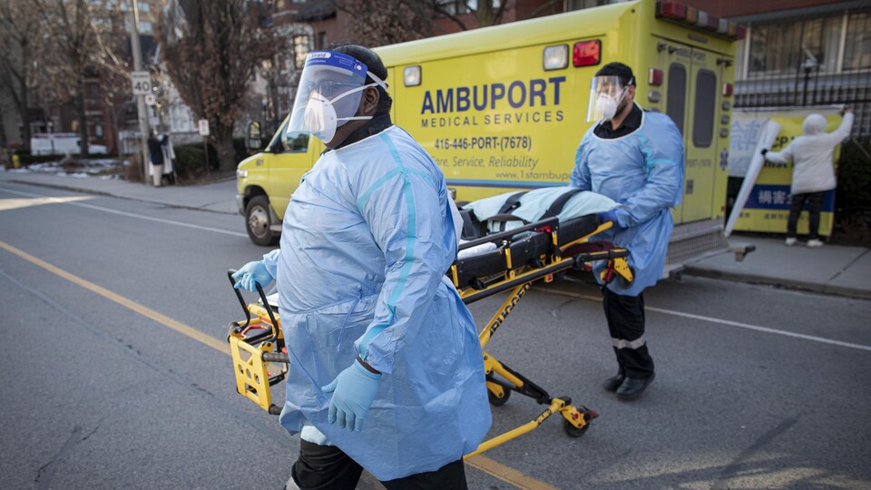 Des préposés qui portent de l'équipement de protection s'apprêtent à transporter un patient d'un foyer de soins à Toronto.