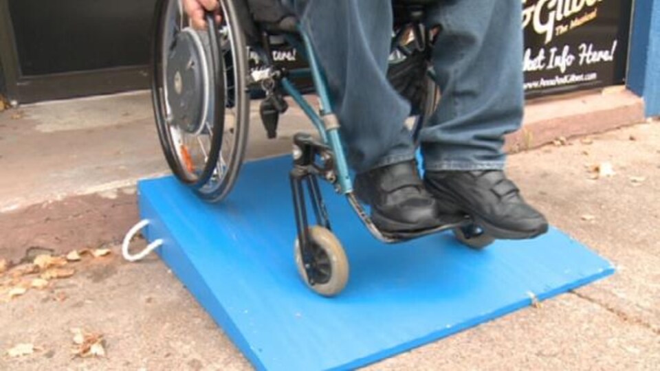 Une personnes en fauteuil roulant descend une rampe d'accès installée devant un magasin.