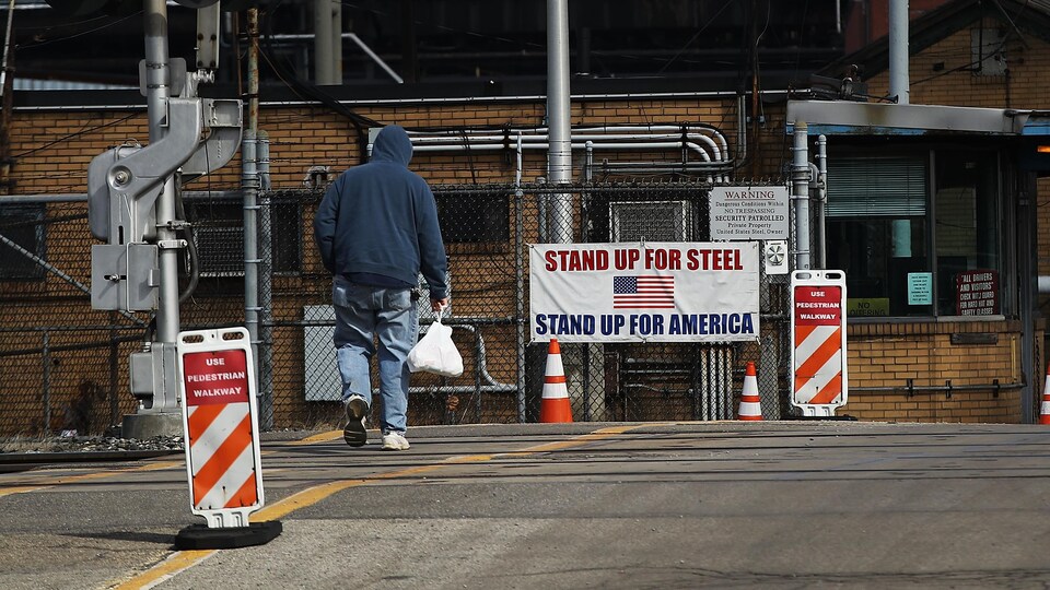 Un travailleur marche vers une affiche écrite en anglais disant « Stand Up for Steel, Stand Up for America ».